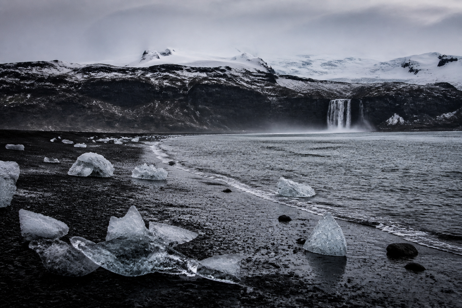 Ice formations on a dark volcanic winter coast beneath a glacier