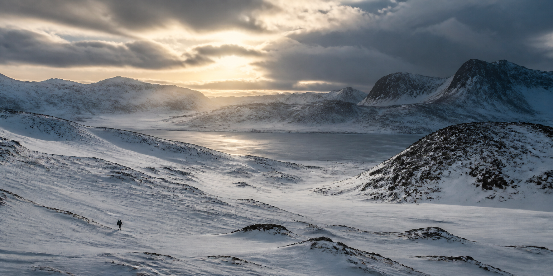 A lone traveller crossing a vast, snow-covered mountain valley beside a frozen lake